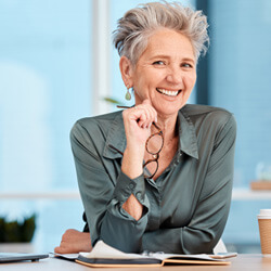 A businesswoman sitting at her desk, smiling, and holding a pair of glasses