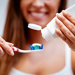 Woman in background squeezing toothpaste onto toothbrush in foreground