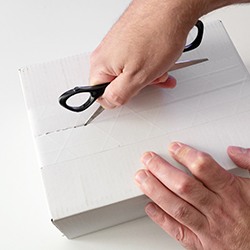 Closeup of hands using scissors to open a white box