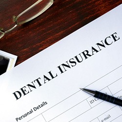 A dental insurance form set on a brown, wooden desk