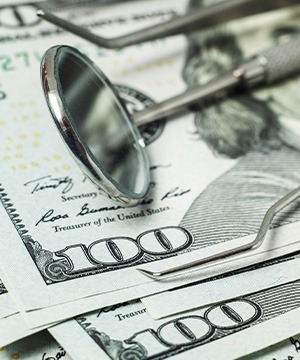 Dental tools laying on a pile of hundred-dollar bills